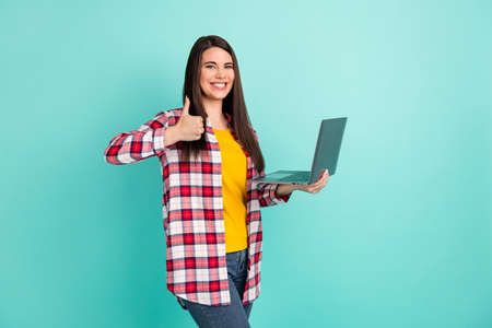 Photo of joyful happy young lady make thumb-up recommend quality hold laptop isolated on teal color backgroundの写真素材