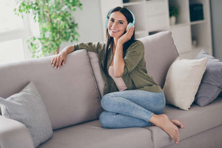 Full body profile side photo of young attractive woman happy positive smile listen music headphones sit sofa home comfortの写真素材