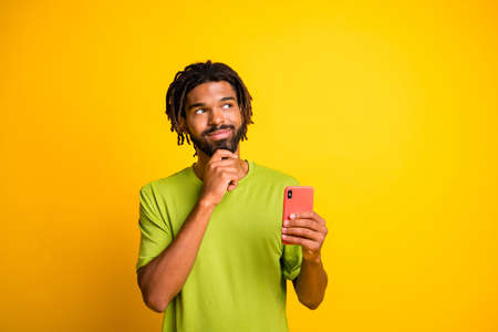 Minded dark skin guy touch chin hand look copyspace think use smartphone wear t-shirt isolated...