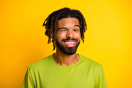 Portrait of nice satisfied dark skin guy wink eye in camera isolated over vibrant yellow color backgroundの写真素材
