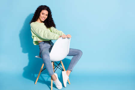 Photo of flirty girlish lady sit chair wait shiny white smile wear pullover jeans isolated blue backgroundの写真素材