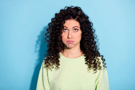 Photo of bored tired lady puffed cheeks look up empty space wear green sweater isolated blue backgroundの写真素材