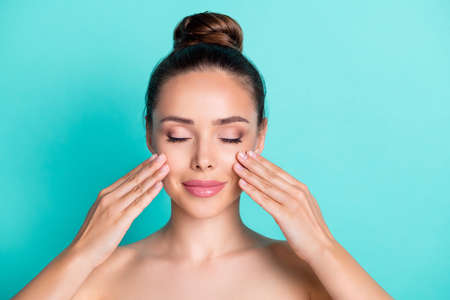Photo of young beautiful dreamy lovely woman with naked shoulders apply anti age cream isolated on teal color backgroundの写真素材