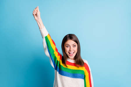 Portrait of delighted young girl raise arm fist holding open mouth wear pullover isolated on blue color backgroundの写真素材