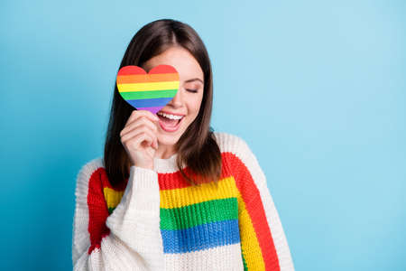 Photo of dreamy sweet young woman dressed striped sweater cover eye colorful heart smiling empty space isolated blue color backgroundの写真素材