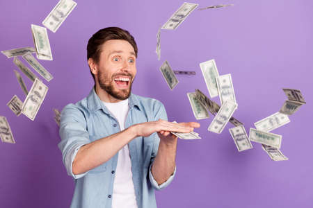 Photo of cool funky young man wear jeans shirt dark throwing big amount money isolated violet color backgroundの写真素材