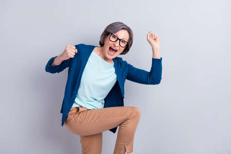 Photo portrait of senior business woman wearing spectacles gesturing like winner isolated on grey...