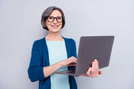 Photo of charming nice attractive old woman hold hands laptop smile wear glasses isolated on grey color backgroundの写真素材