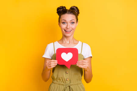 Photo of excited cheerful lady hold red like button open mouth wear green overall isolated yellow...