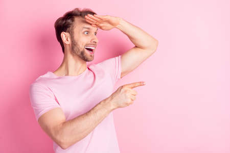 Photo of cool excited young guy wear casual clothes arm forehead looking far away pointing empty space isolated pink color backgroundの写真素材