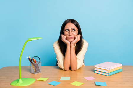 Photo of tired bored young businesswoman look empty space sit table bad mood isolated on pastel blue...