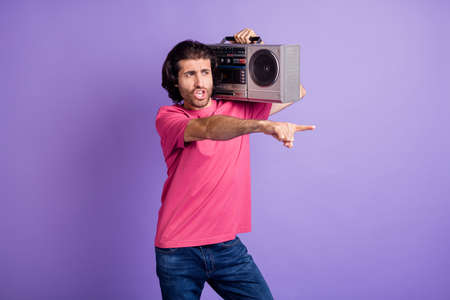 Photo of funky crazy young guy dressed pink outfit dancing holding boom box pointing finger isolated purple color backgroundの写真素材