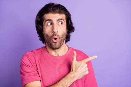 Photo of impressed funky young man wear pink t-shirt looking pointing empty space isolated violet color backgroundの写真素材