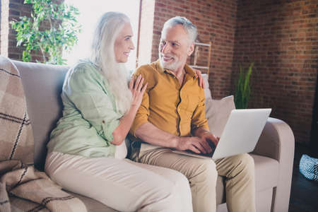 Photo off happy positive old people sit sofa good mood sit couch use laptop indoors inside house...