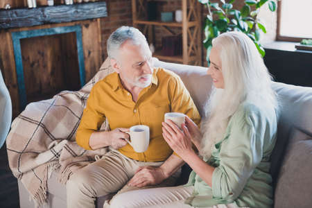 Photo of positive charming man and woman old people good mood sit sofa drink tea indoors inside...