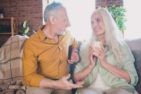 Photo of old pretty adorable grandmother grandfather sitting sofa drinking tea talking indoors flat...