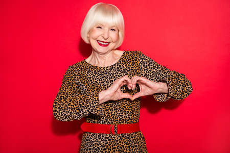 Photo of cheerful sweet adorable old woman hold hands fingers heart shape isolated on red color...