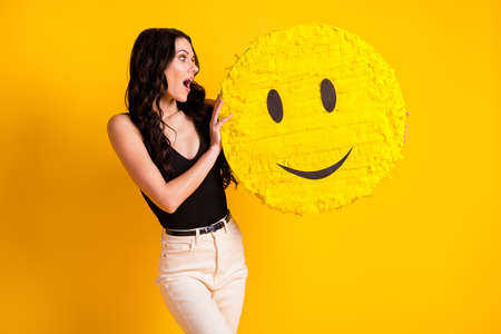 Photo of young woman amazed shocked surprised look hold paper pinata emoji smile isolated over yellow color backgroundの写真素材
