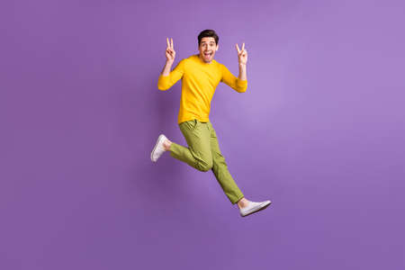 Full size profile side photo of young man happy positive smile jump show peace cool v-sign isolated over purple color backgroundの写真素材