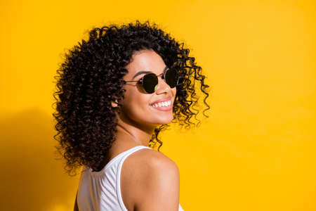Turned photo of charming afro american woman happy smile wear white tank-top isolated on vibrant yellow color backgroundの写真素材
