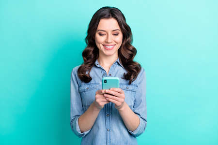 Photo of pretty shiny young woman wear jeans shirt typing modern device smiling isolated turquoise color backgroundの写真素材