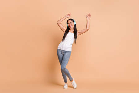 Full length photo portrait of girl in earphones dancing isolated on pastel beige colored background
