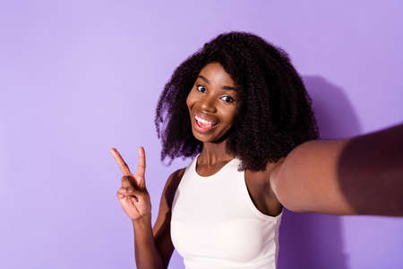 Portrait of cheerful dark skin lady make selfie fingers show v-sign toothy smile isolated on purple...