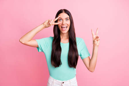 Photo of young excited crazy smiling cheerful positive funky girl showing v-sign isolated on pink...
