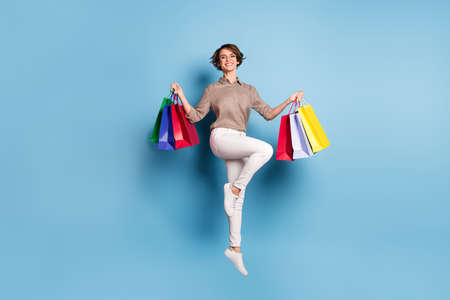 Full size photo of brunette bob haired girl jump hold bags wear plaid shirt white pants isolated on blue color backgroundの写真素材