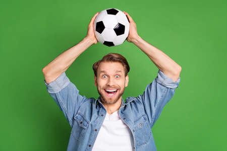 Photo portrait of football fan keeping soccer ball smiling amazed isolated bright green color backgroundの写真素材