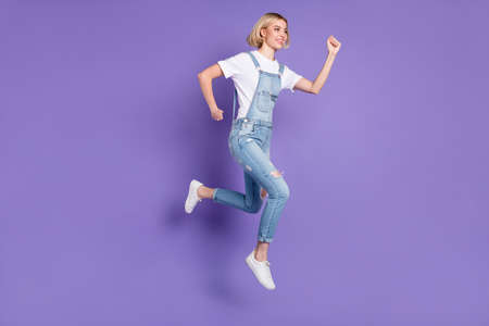 Full size profile photo of nice optimistic short hairdo blond lady run wear white t-shirt overall isolated on violet backgroundの写真素材