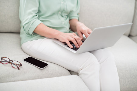 Cropped photo of busy person sit on couch arms hold use laptop working from home free time indoorsの写真素材