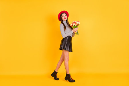 Full size profile side photo of attractive woman walk empty space hold flowers tulips isolated on yellow color backgroundの写真素材