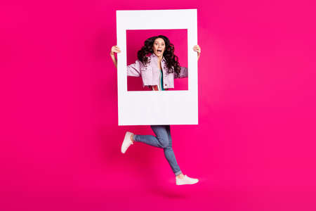Full size photo of young happy positive crazy girl running in air with huge white frame in hands isolated on pink color backgroundの写真素材