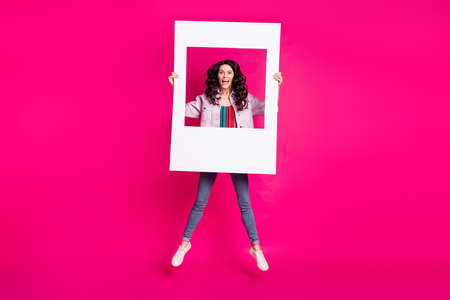 Full size photo of young funky funny smiling excited girl jumping with big white frame isolated on pink color backgroundの写真素材
