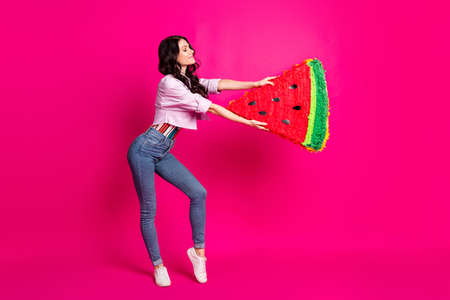 Full length photo of pretty shiny young lady dressed jeans jacket holding big watermelon slice isolated pink color backgroundの写真素材