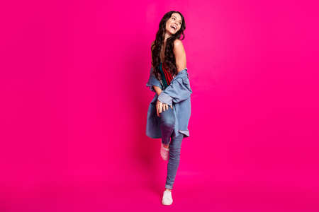 Full length photo of cute charming young woman wear jeans jacket walking laughing isolated bright pink color backgroundの写真素材