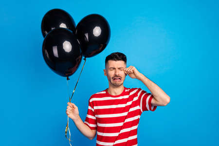 Photo of unhappy upset young man cry hold balloons bad mood isolated on pastel blue color backgroundの写真素材