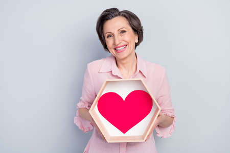 Photo of confident cheerful mature lady wear pink clothes holding big red heart smiling isolated grey color backgroundの写真素材
