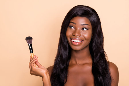 Photo of dreamy girlish brunette charming lady hold cosmetic brush look up empty space isolated beige backgroundの写真素材