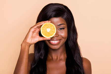 Photo of cheerful pretty lady hold orange slice cover eye toothy shiny smile look camera isolated beige backgroundの写真素材