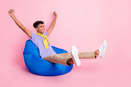 Full size photo of young happy cheerful smiling african man sit armchair raise fists in victory isolated on pink color backgroundの写真素材