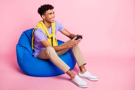Full body profile side photo of young black man happy smile play game joystick sit chair isolated...
