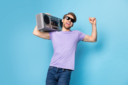 Photo portrait of young man in black sunglass keeping boombox dancing isolated on pastel blue color backgroundの写真素材
