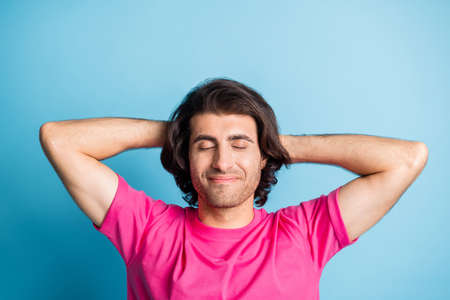 Young man look satisfied relaxed hands behind head closed eyes in pink outfit isolated on blue color backgroundの写真素材