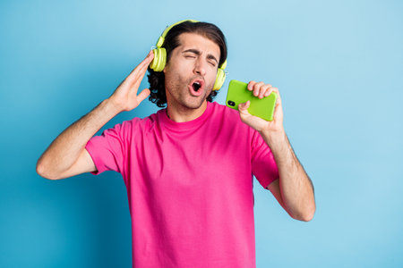 Portrait of funky guy holding device like mic listening singing pop single having fun isolated over...