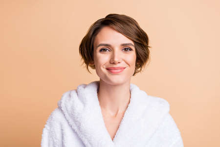 Close-up portrait of nice attractive cheery girl wearing white bathrobe isolated over beige pastel color backgroundの写真素材