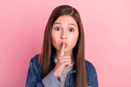 Photo portrait of small girl put finger near lips keeping secret isolated on pastel pink color...