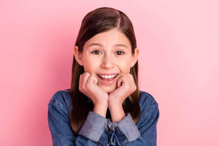 Photo portrait of little girl cute sweet smiling touching cheeks isolated on pastel pink color backgroundの写真素材
