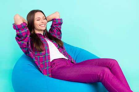 Portrait of attractive dreamy cheerful girl lying in bag chair sleeping isolated over bright teal color backgroundの写真素材
